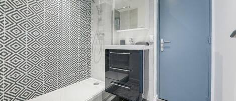 A modern bathroom with a geometric patterned wall, a built-in shower, and a blue door.