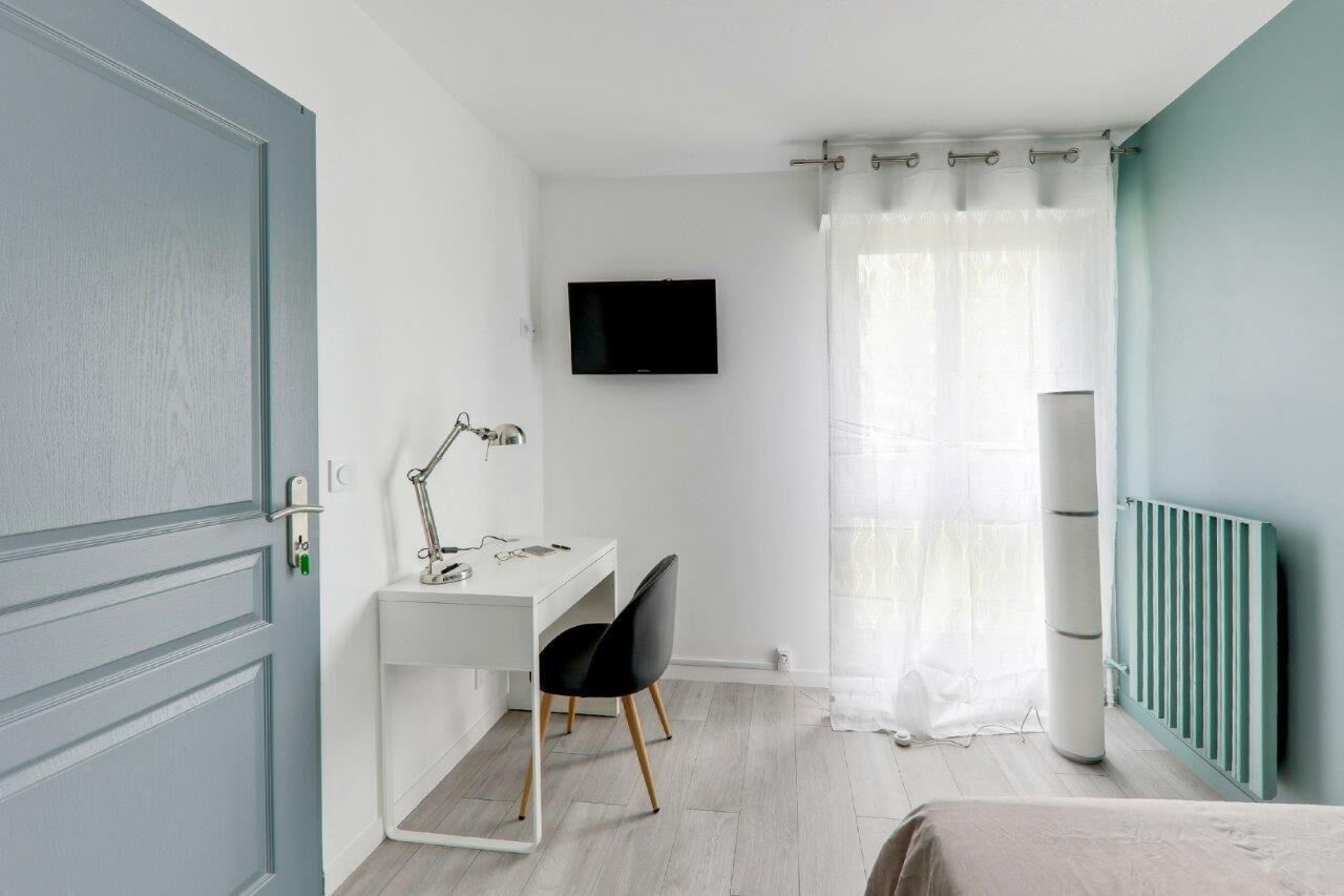 Un dormitorio con una cama, un escritorio con silla, un televisor y un radiador.