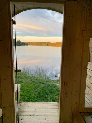 Une porte en bois ouverte donne sur un paysage paisible : un lac tranquille bordé d’une zone herbeuse.