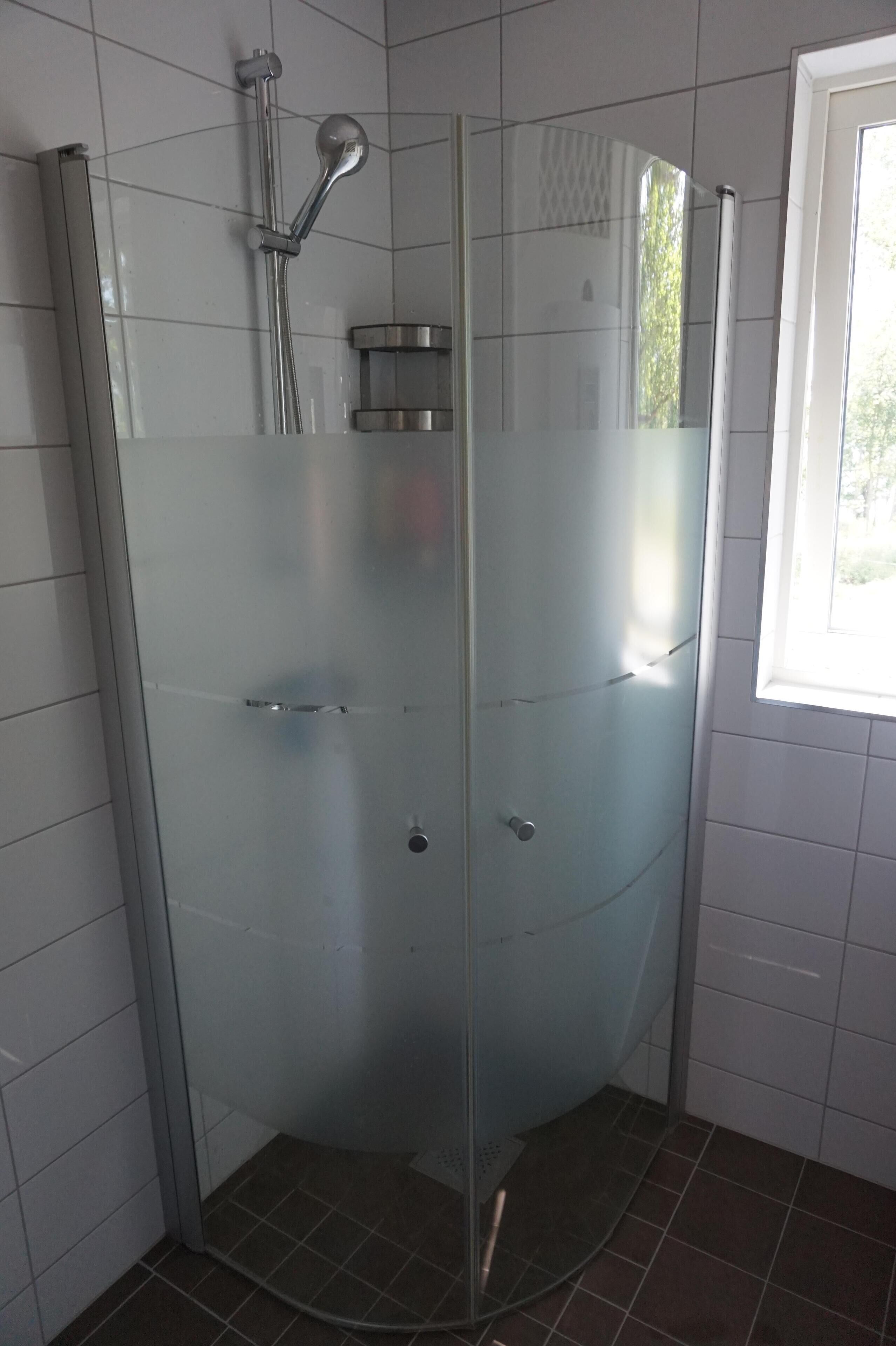 Een douchecabine met glazen wanden, een handdouche, bedieningspaneel en een klein plankje.