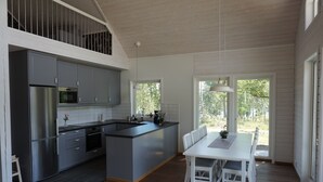 A modern kitchen with grey cabinets, a stainless steel refrigerator, and a dining area with a white table and chairs. - Lövanäs Newly built modern house in a secluded location directly on the lake with its own jetty, boat (Korsberga)