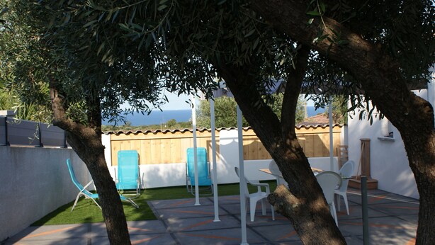 Terrassa exterior amb vista al mar, amb taula i cadires blanques, una cadira blava i una tanca de fusta.
