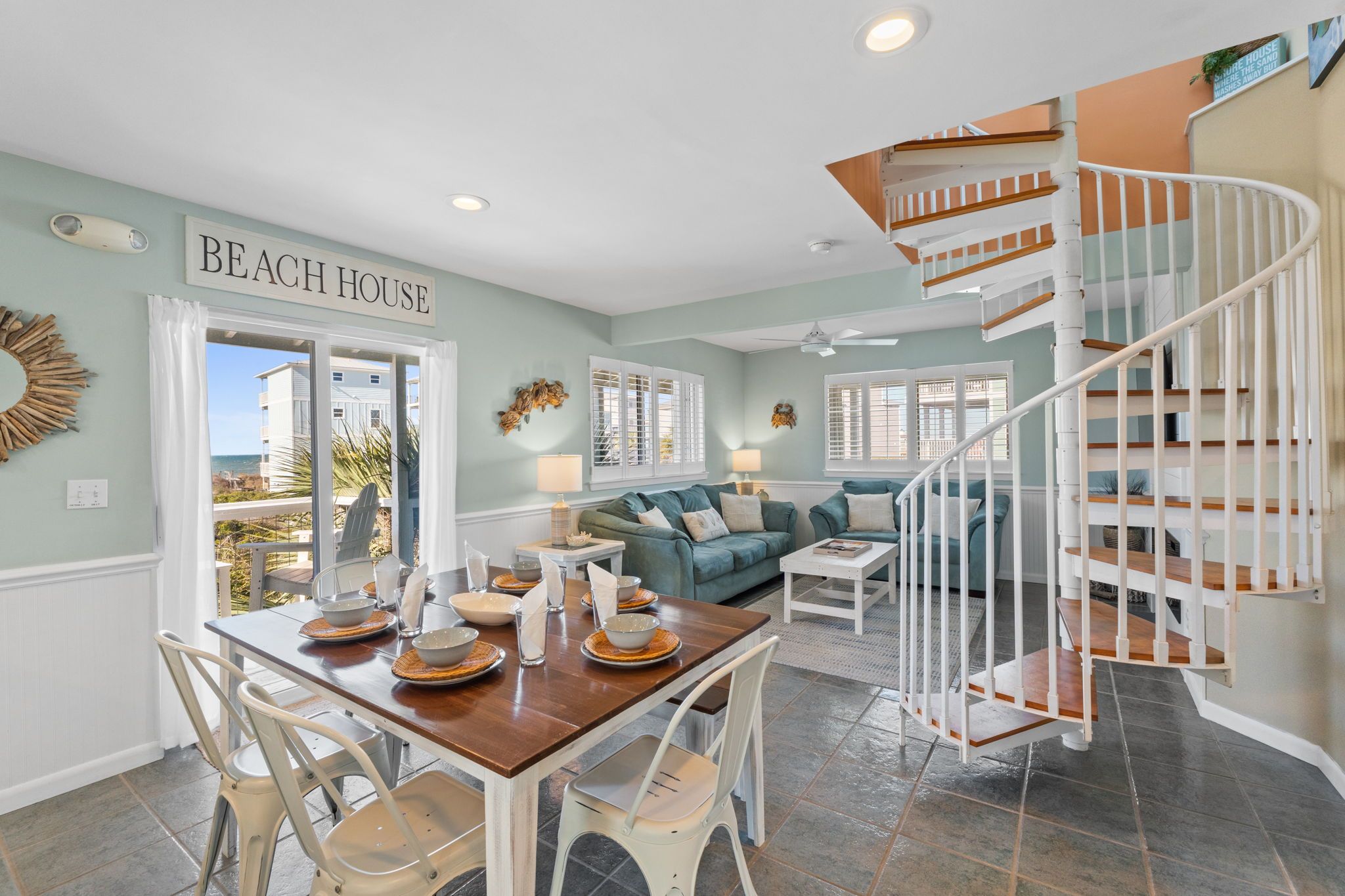 A dining area with a table set for four, a staircase, and a view of the ocean.