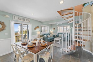 A dining area with a table set for four, a staircase, and a view of the ocean.