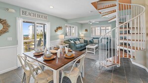 A dining area with a table set for four, a staircase, and a view of the ocean.