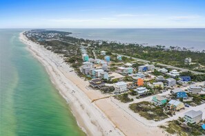 An aerial view of a coastal area with a beach, houses, and a pier.