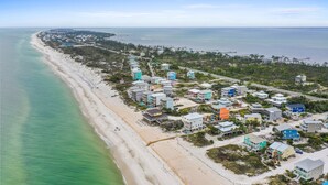 An aerial view of a coastal area with a beach, houses, and a pier.