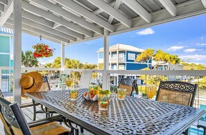 A covered outdoor seating area with a table, chairs, and hanging flower baskets.
