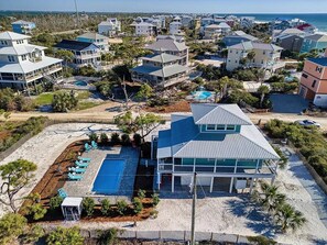 An aerial view of a coastal residential area with multiple houses, a large swimming pool, and a beach.