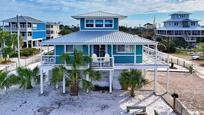A beachfront house with a prominent tower, a covered porch, and a sandy beach area.