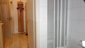 Et badeværelse med en glasbrusekabine, hvid klinkevæg og en metalreol.