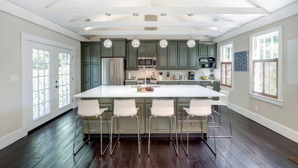 A spacious kitchen with a central island, white bar stools, and green cabinets. - 1828 Cottage | Heated Pool in Private Garden | Sleeps 6 | Pets | On-Site Parking (Savannah)