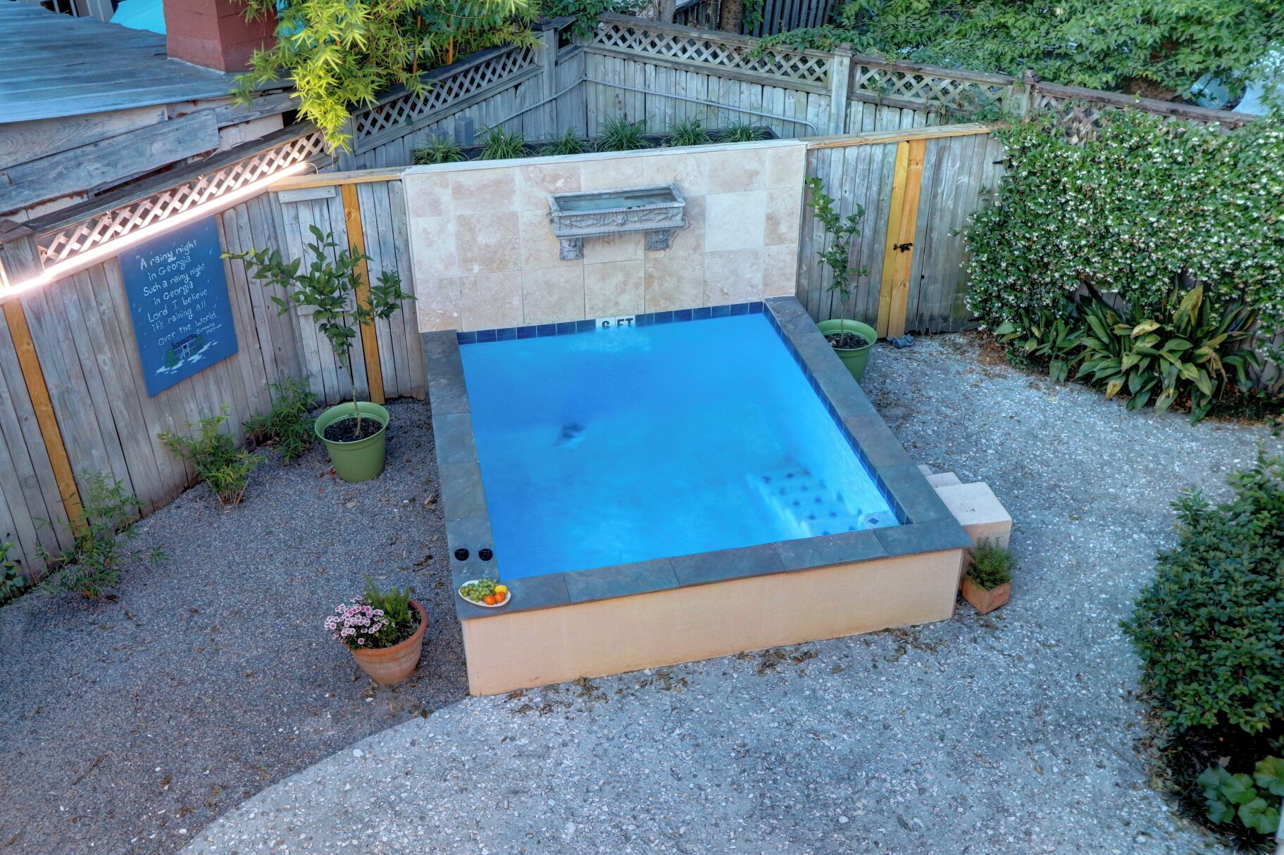 Un bain à remous entouré de pierres, une terrasse en bois et un petit jardin agrémenté de plantes en pot.