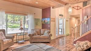 A spacious living room with a wooden ceiling, a sofa set, a coffee table, and a large window offering a view of the outdoors. - Casa Immaculata on Chalk Creek w/ Views! (Nathrop)