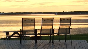 A wooden deck with three chairs facing a body of water at sunset. - Charlottetown Hrbr’view Executive Waterfront (Stratford)