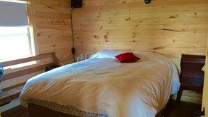 A wooden cabin bedroom with a bed, a red pillow, a nightstand, and a window. - Charlottetown Hrbr’view Executive Waterfront (Stratford)