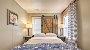 Un dormitorio con cama, dos lámparas de noche, una ventana con cortinas a rayas y un panel de pared de madera.