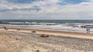 Una playa con arena, algunas personas y unas cuantas sillas de playa.