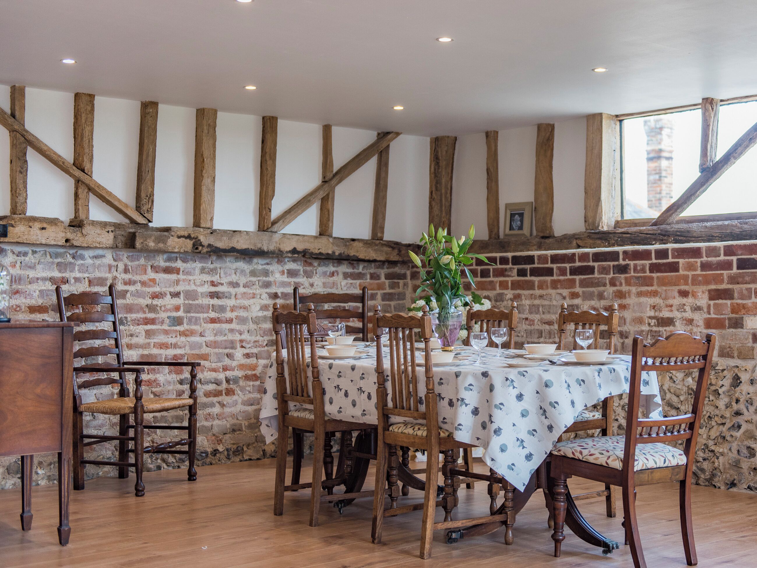 Un coin repas avec un mur en briques, des poutres en bois et une table dressée pour six personnes.