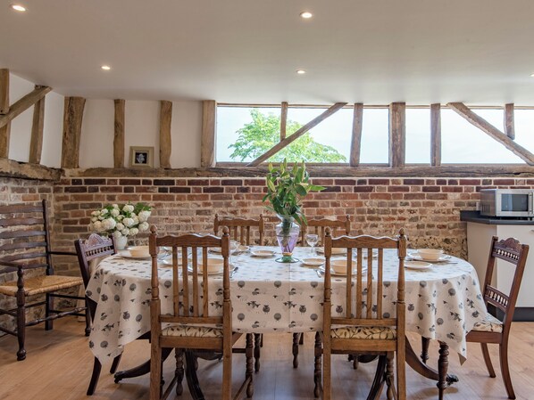 A dining area with a brick wall, wooden beams, and a large window. - 3 bedroom accommodation in Wormshill (Wormshill)