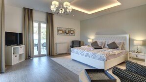 Un dormitorio moderno con una cama grande, un televisor sobre un mueble, una araña y vistas del exterior a través de una puerta corrediza.