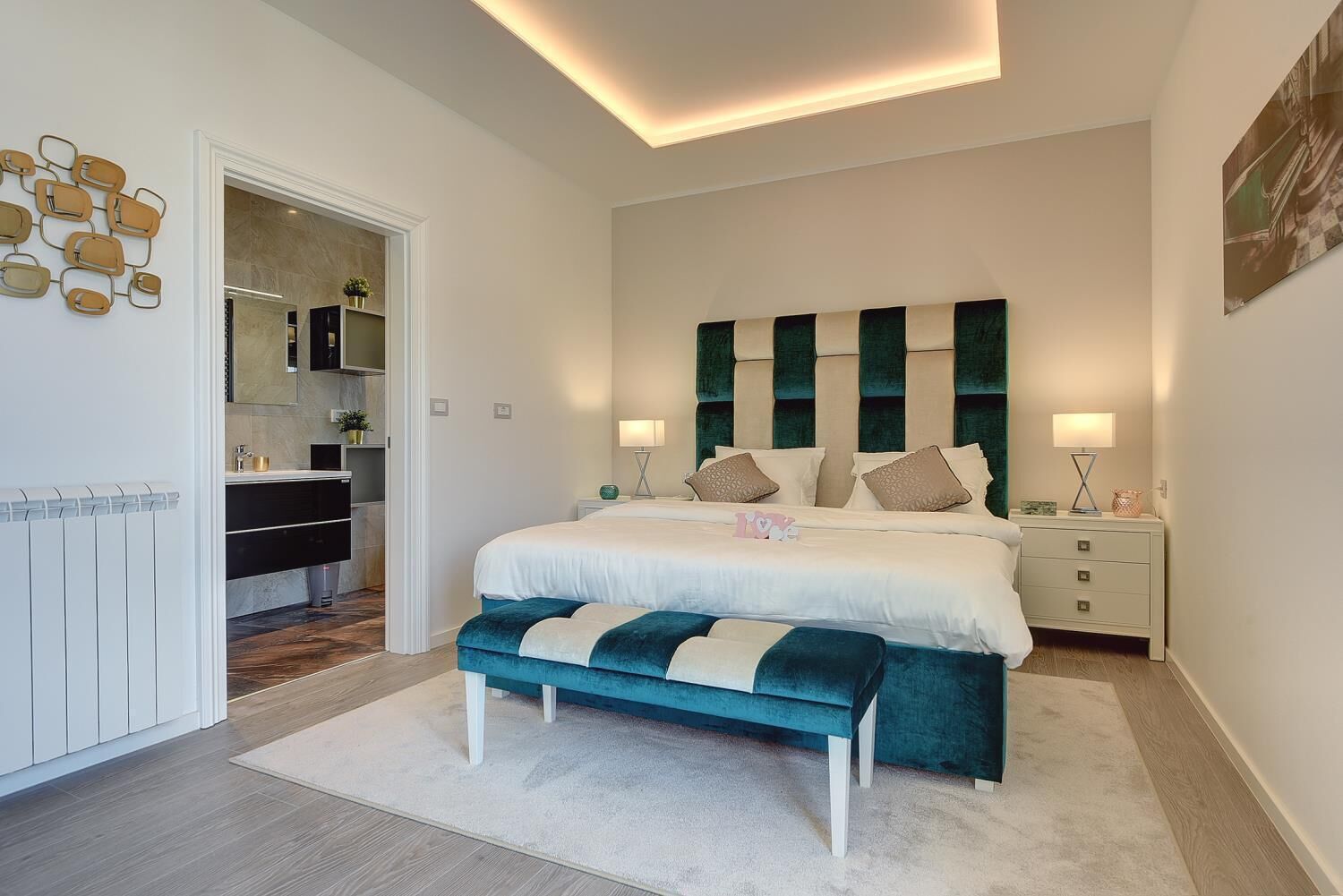 Een moderne slaapkamer met een groot bed, een bankje en een nachtkastje met lampen.