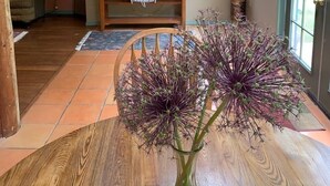 Ett träbord med en vas med blommor i mitten, en bänk med en lampa och en dörr med fönster i bakgrunden.