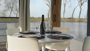 A table set for two with a bottle of champagne, glasses, and cutlery on a deck overlooking a body of water. - Cozy ship in Nieuwpoort with WiFi (Nieuwpoort)