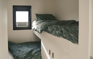 Ein kleines Zimmer mit einem Einzelbett, einem Fenster und einem Einbauschrank.