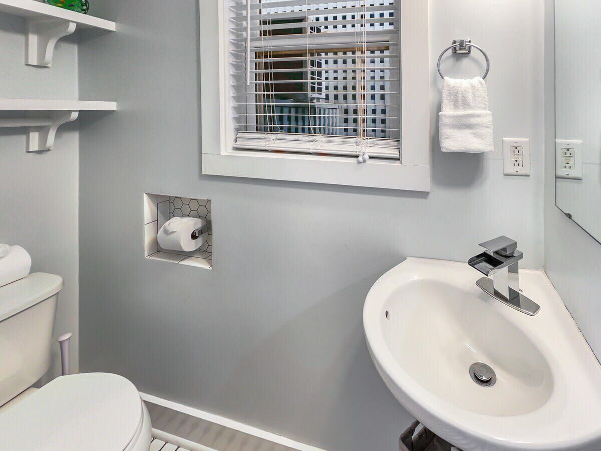 Une salle de bain comprenant des toilettes, un lavabo, une fenêtre avec des stores et un porte-serviettes.
