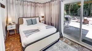 Ein Schlafzimmer mit einem großen Bett, einem Nachttisch, einer Lampe und Blick auf die Außenpatio.