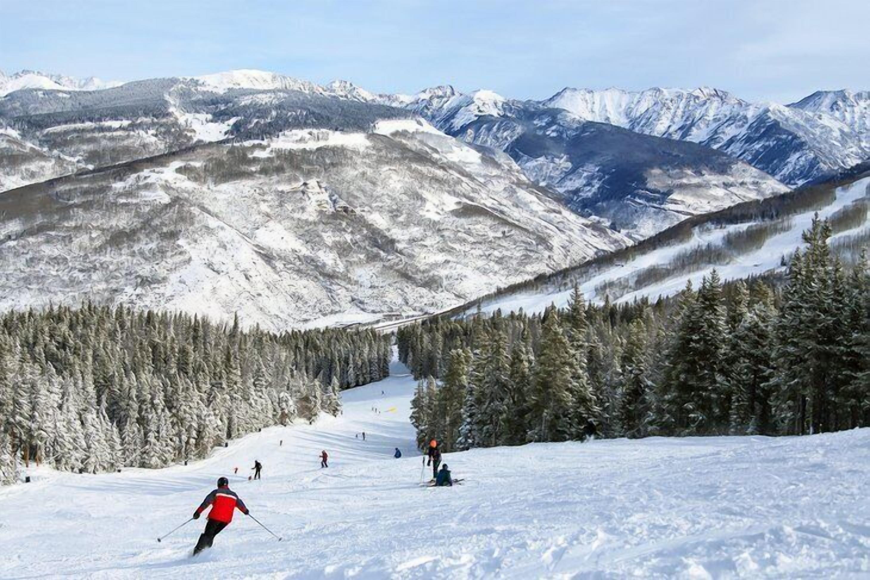 Un paysage de montagne enneigé avec des skieurs et une vue dégagée sur les montagnes lointaines.