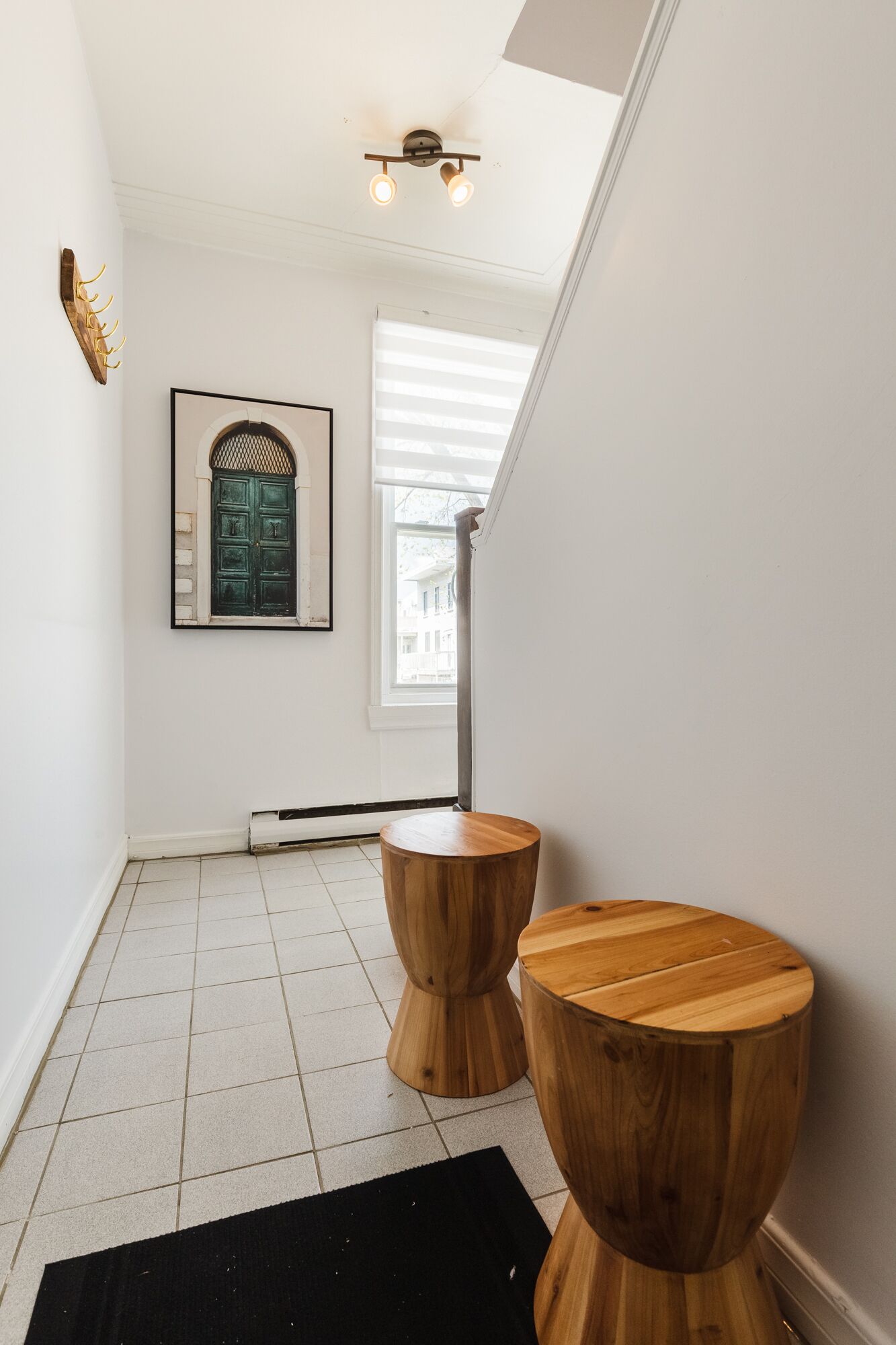 A hallway with white walls, a framed artwork, a green door, and two wooden stools.