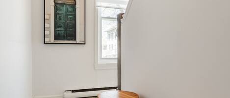 A hallway with white walls, a framed artwork, a green door, and two wooden stools.
