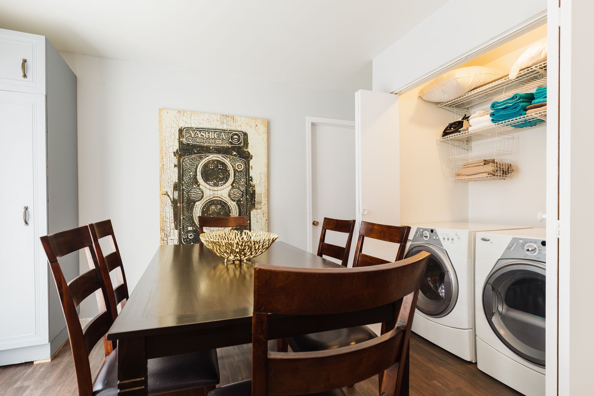 A dining area with a table and chairs, a washing machine, and a laundry basket.