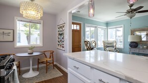 A kitchen with white cabinets, a white island, a chandelier, and a ceiling fan. - Charming Ventura Beach Bungalow on Prime Beach Lane in Pierpont by the Sea (Ventura)