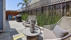 A patio area with wicker furniture, a grill, and a wooden fence. - Charming Ventura Beach Bungalow on Prime Beach Lane in Pierpont by the Sea (Ventura)