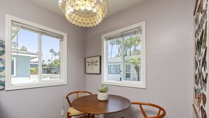 A dining area with a round table, two chairs, a hanging light fixture, and a window with blinds. - Charming Ventura Beach Bungalow on Prime Beach Lane in Pierpont by the Sea (Ventura)