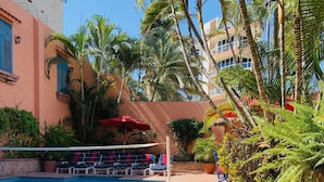 A pool area with steps leading down to the water, surrounded by palm trees and a building with a red and white facade. - Spectacular Casa Coco, Private Beachfront Villa in Vallarta/Bucerias, Mexico (Bucerías)