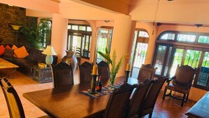 A dining area with a wooden table, chairs, and a vase with a candle. There is a sofa and a lamp in the background. - Spectacular Casa Coco, Private Beachfront Villa in Vallarta/Bucerias, Mexico (Bucerías)