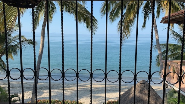A beach view through a metal railing with palm trees and a thatched structure. - Spectacular Casa Coco, Private Beachfront Villa in Vallarta/Bucerias, Mexico (Bucerías)