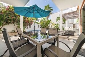 Eine Terrasse im Freien mit einem Tisch mit Glasplatte, Stühlen und einem blauen Sonnenschirm.