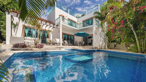 Un bâtiment moderne à deux étages doté d’une piscine, d’un espace extérieur aménagé et d’une végétation tropicale luxuriante.