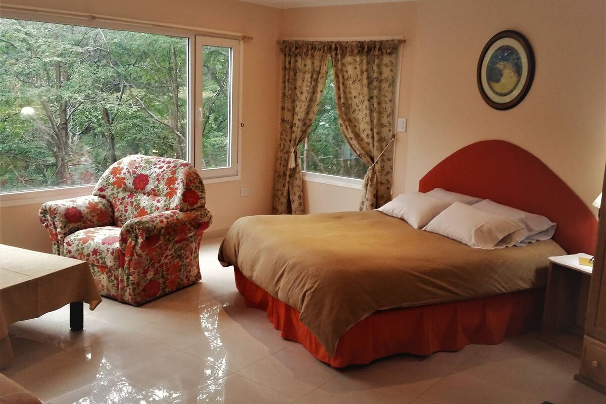 A bedroom with a bed, a chair, a table, and a window with curtains.