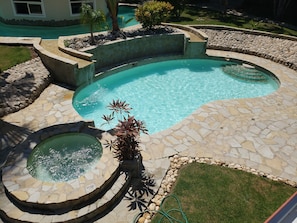A swimming pool with a stone border and a small hot tub, surrounded by a landscaped garden with rocks and plants. - Villa Dove of Grace (Sosúa)
