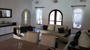 Ein geräumiges Wohnzimmer mit hoher Decke, einer Sofagarnitur, einem Esstisch und einer Küchenzeile.