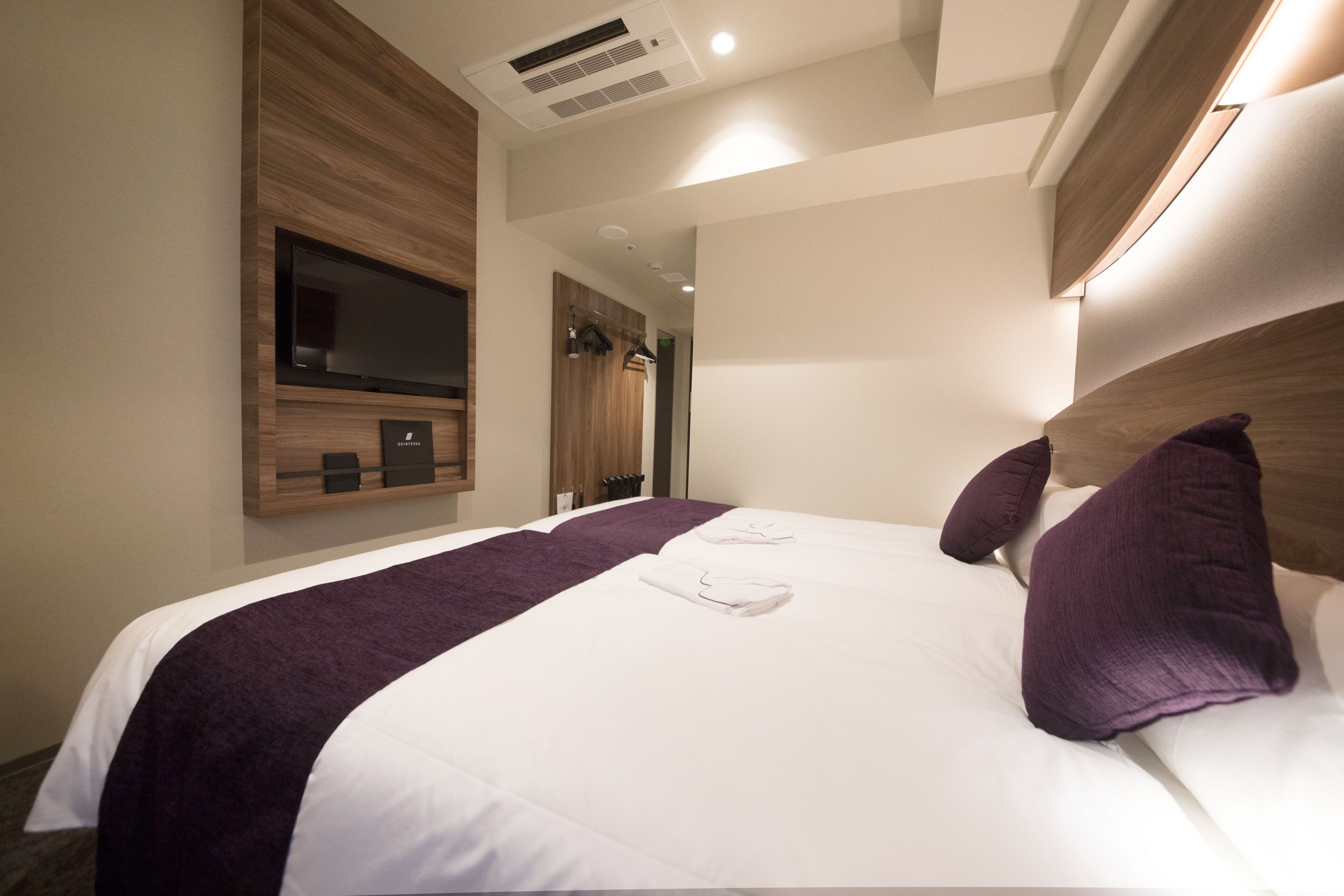 A hotel room with a large bed, a flat-screen TV mounted on the wall, and a wooden headboard.
