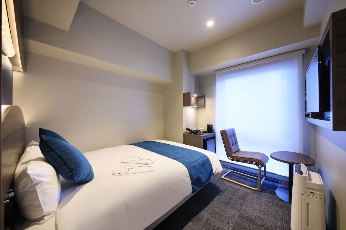 Une chambre d’hôtel avec un lit, un bureau, une chaise, une petite table et un téléviseur.