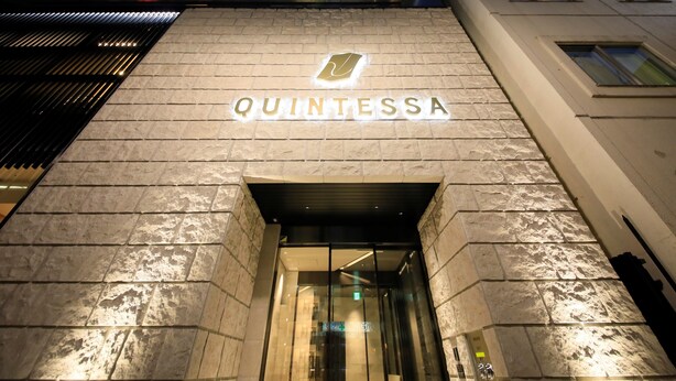 Exterior del hotel Quintessa, con un llamativo letrero iluminado y una entrada moderna.
