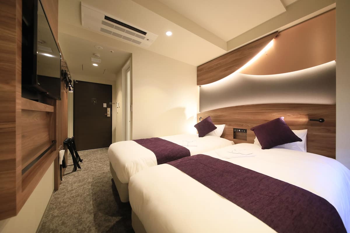 Une chambre d’hôtel avec deux lits, un téléviseur à écran plat, une tête de lit en bois et un sol recouvert de moquette.